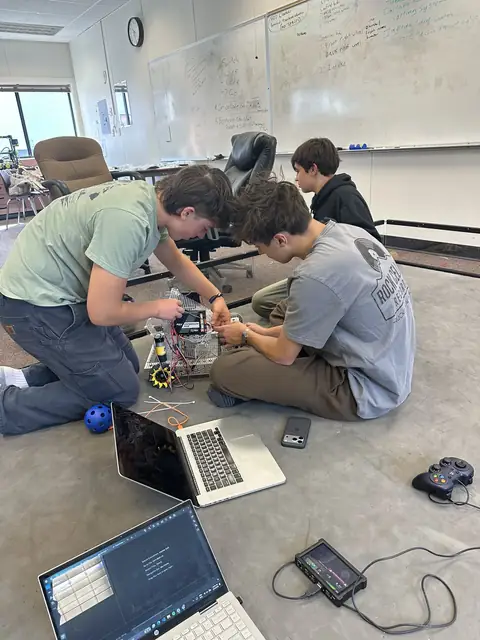 Team members building and testing the robot, with laptops and a game controller on the floor.